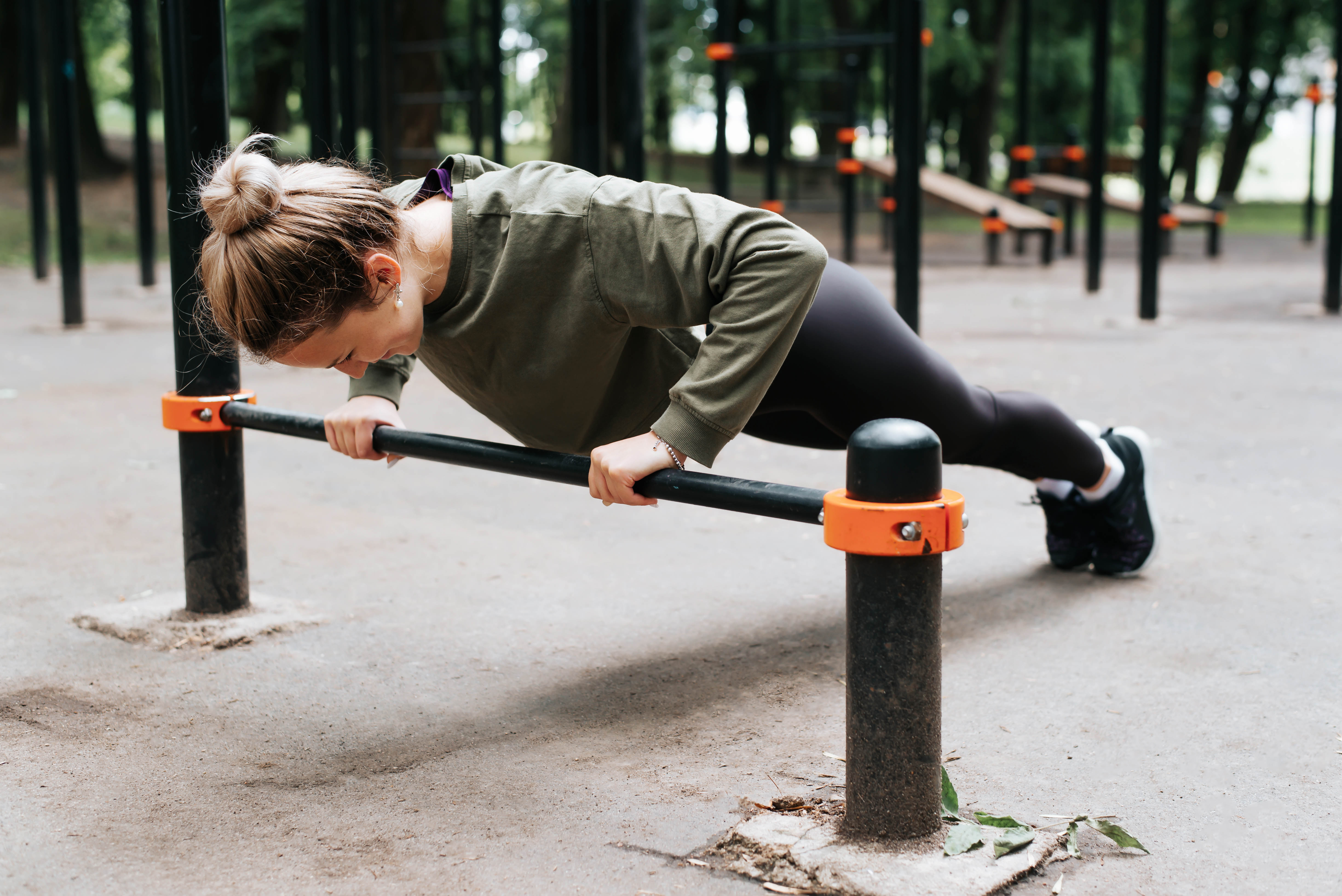 Young ,active woman completes push-ups using a bar installed in an outdoor workout space